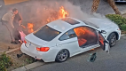 A police officer and bystander pull a driver from an enflamed car
